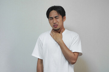 An Asian man in a white t-shirt is holding his throat, indicating pain or discomfort.