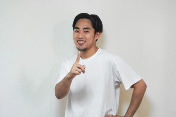 A man in a white t-shirt points directly at the viewer with a confident smile.