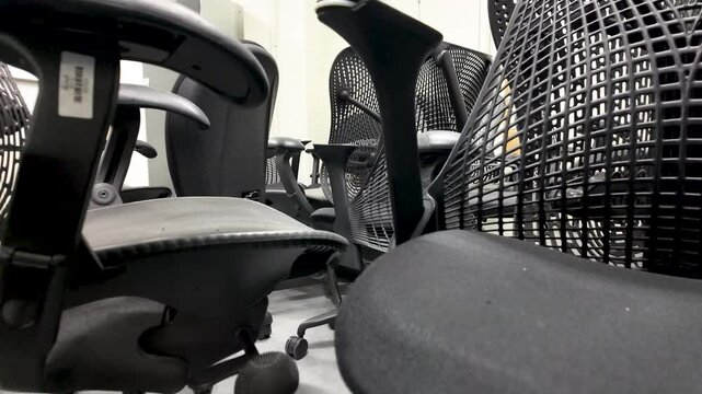 Discarded office chairs are seen piled up in a basement storage room, representing concepts of waste, obsolescence, and office furniture disposal