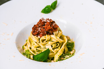 Fituccini with balognese sauce and bisilican in a white wide-brimmed plate. Close-up. Italian menu.
