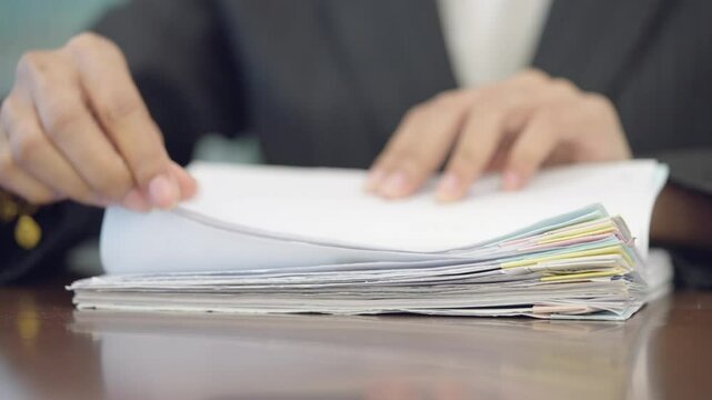 A person is writing on a piece of paper. The paper is open and has a lot of writing on it