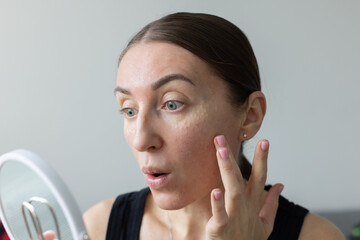 Shocked woman looking at the mirror how looks her face after cosmetology procedures.