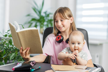 Baby chewing pen while sister reads book