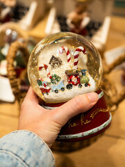 A person is holding a vibrant snow globe filled with a miniature Christmas scene. Inside, a...