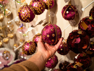 A hand holds a vibrant purple ornament adorned with gold embellishments. Surrounding decorations...
