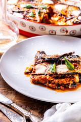 Eggplants alla parmesano on a white plate on a wooden table with a white napkin. Baked eggplants with tomatoes and cheese according to a traditional Italian recipe