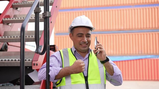 Engineer foreman talking on the phone receiving good news for success project at container warehouse, supervisor working at dock standing at forklift. Logistics terminal