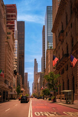 New York City street landscape with high-rise buildings, cars, and American flags along Fifth Avenue in Upper Manhattan — a vintage-style photo at sunrise on a quiet Sunday morning.