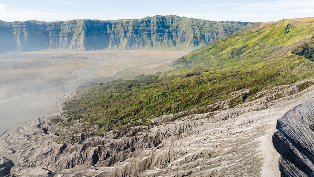 Aerial view of the Bromo-Tengger-Semeru National Park's stark volcanic landscape meets vibrant green vegetation in a stunning natural contrast, Mount Bromo, East Java, Indonesia.