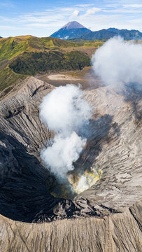 Aerial view of the volcanic crater, where wisps of white smoke billow against the stark, gray landscape, Mount Bromo Volcano, East Java, Indonesia.