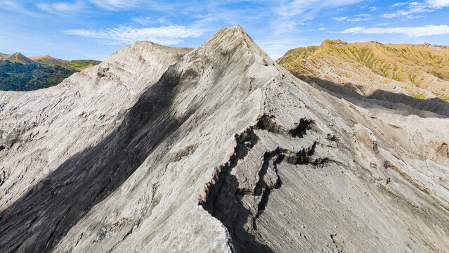 Aerial view of rugged, grey volcanic peaks rise sharply against the blue sky, showcasing the stark beauty of Mount Bromo Volcano, East Java, Indonesia.