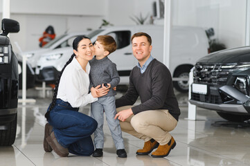 Happy parents with small kid after receiving keys for their new car in a showroom
