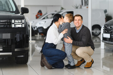 Young happy family enjoying while buying a new car in a showroom