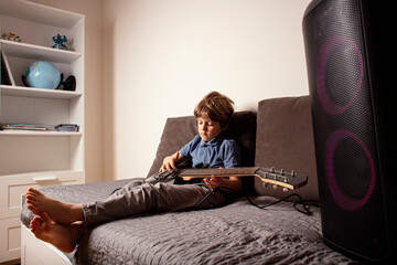 Young boy playing electric guitar at home, learning music and practicing concentration. The child appears focused and relaxed, suggesting a music practice or learning moment. Play music at home.