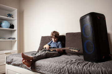 Young boy playing electric guitar at home, learning music and practicing concentration. The child appears focused and relaxed, suggesting a music practice or learning moment. Play music at home.