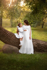 A cute little girl holds her mother's pregnant belly. The family is dressed in white clothes in...