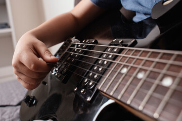 Close-up of a child&rsquo;s hand playing electric guitar. Focus on guitar strings and fretboard. Concept of music, learning, talent, and childhood creativity. Teaching music. Kid with a guitar.