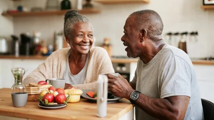 Senior African American couple enjoying morning breakfast at home. Sharing warm drinks and fresh food in kitchen. Happy elderly pair starting their day together. Cozy domestic morning routine. - Powered by Adobe