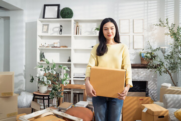 Asian woman holding cardboard box after packing stuff for moving house. Concept of new beginning,...