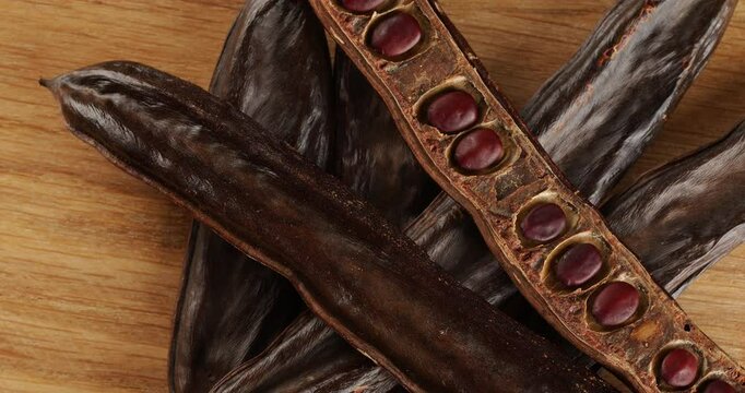Carob pods on a wooden board top view, on a rotating table.