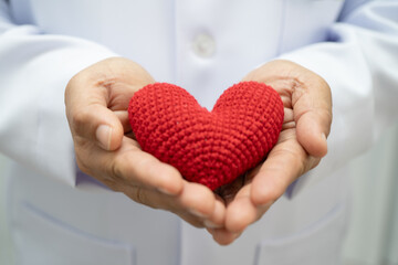 Asian woman doctor holding red heart for health in hospital.