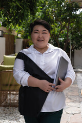 Young plus size Asian woman working on laptop outdoors at a cafe in sunny weather