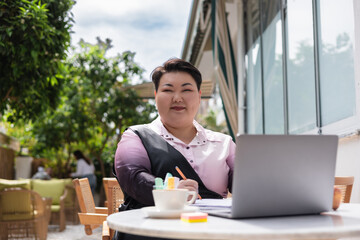 Young plus size woman working outdoors on laptop at cafe during the day