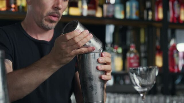 Handheld shot of mature Caucasian tattooed bartender shaking cocktail in modern bar