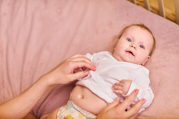 Young woman with brown braids, caucasian, showing affection to baby girl on pink bed. Warm lighting...