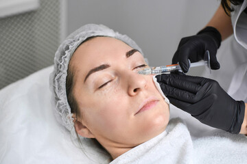 Female patient undergoes cosmetic injection by professional in clinical environment. Setting is serene and sterile, emphasizing precision and care in aesthetic treatments