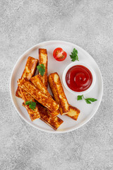 Fried halloumi cheese sticks with tomato sauce on a white plate on a concrete background.