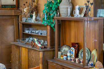 Vintage display cabinets filled with glassware, ceramics, and decorations, including dried plants and an old radio – classic retro interior with a collection of ornaments.