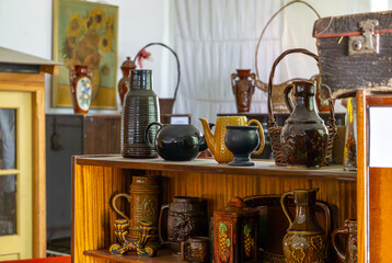 Wooden shelf with a collection of vintage ceramic jugs, mugs, and teapots, set against an interior...