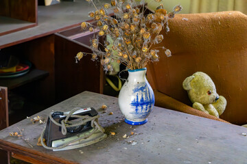 Old iron, vase with dried plants, and a teddy bear on a dusty cabinet – nostalgic scene from an...
