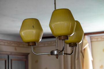 Old ceiling chandelier with yellow glass shades from the communist era, hanging in a neglected...