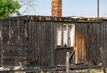 Burned wooden facade of an old building with a broken window and a brick chimney. Visible fire...