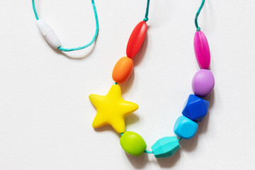 Colorful silicone baby teether necklace featuring various shapes and a star design, intended for soothing teething infants. Bright and engaging, suitable for babies' sensory needs