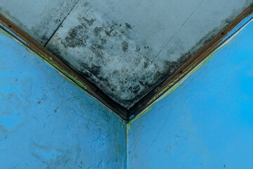 Moldy and damp ceiling corner with black mildew and water damage, cracked wall paint, and signs of...