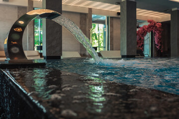 Luxurious indoor pool with hydromassage jets and water spout. Elegant wellness area with modern...
