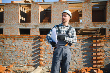An architect or engineer on the construction of brick houses holds the construction plan in his...