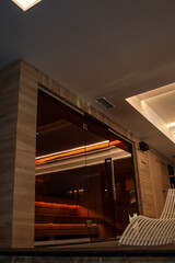 Modern indoor sauna with warm ambient lighting behind glass walls, next to stylish white lounge...