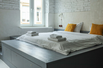 Scandinavian-style bedroom with a gray wooden platform bed, white linens, yellow pillows, and a...