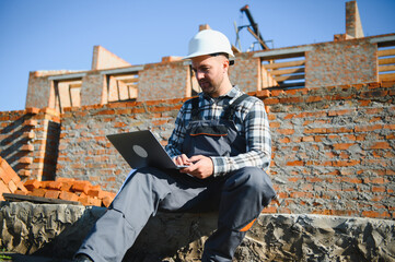 Architect or engineer on construction site with laptop monitoring construction process