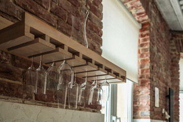 Glassware hanging upside down from a wooden wine glass rack mounted on a rustic brick wall, with...
