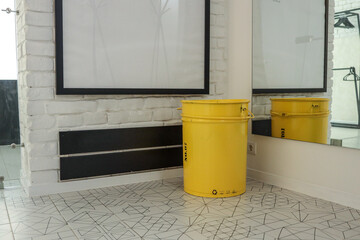 Bright yellow metal bin with recycling symbols placed in a modern interior, near a large wall...