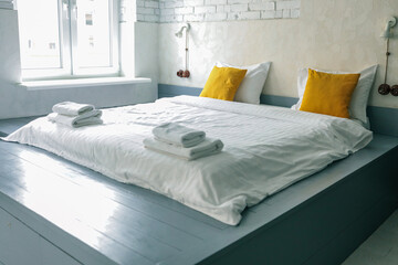 Bright modern bedroom with white brick walls, a large bed with yellow pillows, folded towels, and...
