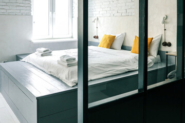 Bright modern bedroom with white brick walls, a large bed with yellow pillows, folded towels, and...