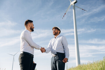 Handshake, successful deal. Two men engineers are in field, with wind turbines
