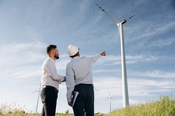 Looking far away, planning. Two men engineers are on field, with wind turbines