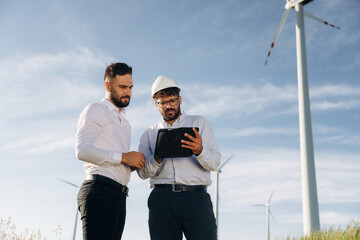 Getting to know the plan. Two men engineers are on field, with wind turbines
